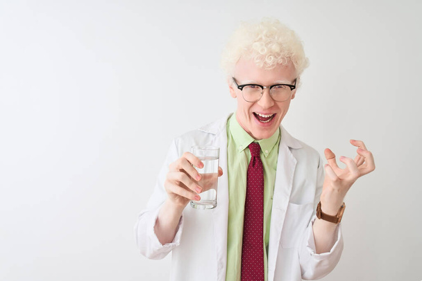 Albino scientist man wearing glasses holding glass of water over isolated white background very happy and excited, winner expression celebrating victory screaming with big smile and raised hands - 写真・画像