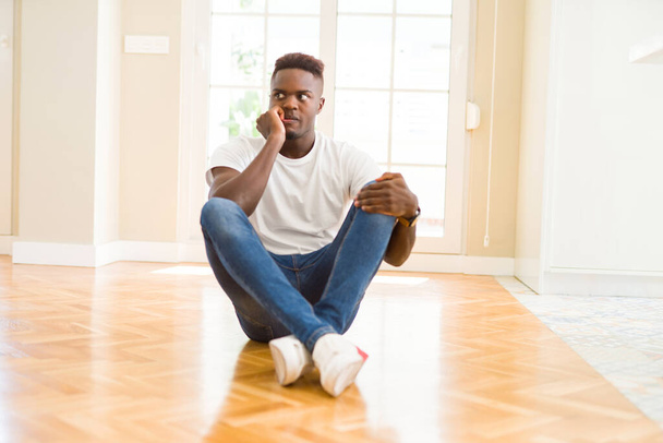 自宅で床の上に座っているハンサムなアフリカ系アメリカ人の男性は、口の爪をかむ上で手でストレスと緊張している。不安の問題. - 写真・画像