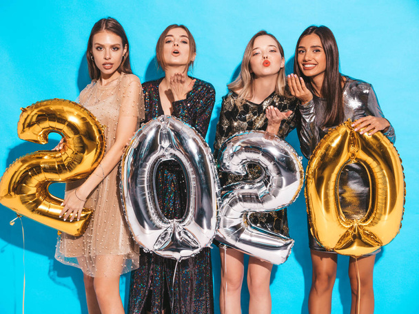 Beautiful Women Celebrating New Year. Happy Gorgeous Girls In Stylish Sexy Party Dresses Holding Gold and Silver 2020 Balloons, Having Fun At New Year's Eve Party. Holiday Celebration.Charming Models  - Valokuva, kuva