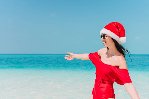 Young woman in Santa Hat walking spread her hands on white sandy beach - Photo, Image