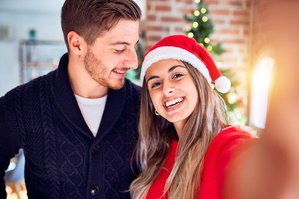 Mladý krásný pár se šťastně a sebevědomě usmívá. Stojící udělat selfie kamerou kolem vánočního stromečku doma - Fotografie, Obrázek