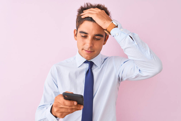 Young handsome businessman using smartphone standing over isolated pink background stressed with hand on head, shocked with shame and surprise face, angry and frustrated. Fear and upset for mistake. - Фото, зображення