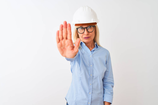Middle age architect woman wearing glasses and helmet over isolated white background doing stop sing with palm of the hand. Warning expression with negative and serious gesture on the face. - Photo, Image