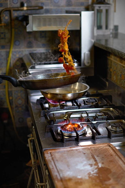 Ruokakäsite. Kokki paistaa pannulla tomaatit, osterit ja oksentaa, valmistaa ruokalajin keittiössä.
. - Valokuva, kuva