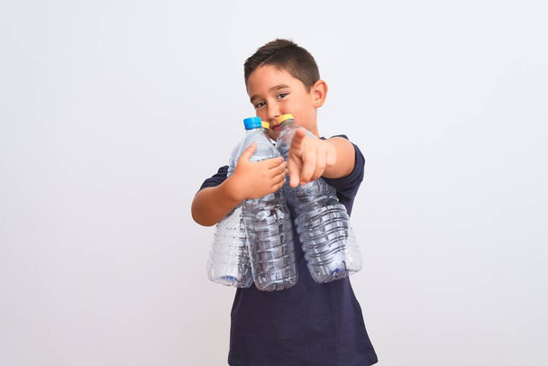 Beautiful kid boy recycling plastic bottles standing over isolated white background pointing with finger to the camera and to you, hand sign, positive and confident gesture from the front - Foto, imagen
