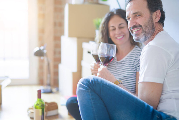 Starší Romantický párek v lásce sedí na podlaze bytu s krabičky a oslavuje pití vína s úsměvem, že se bude stěhovat do nového domova - Fotografie, Obrázek