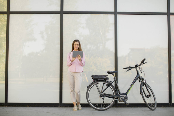 Jeune femme avec tablette et e-bike en plein air le jour ensoleillé
 - Photo, image