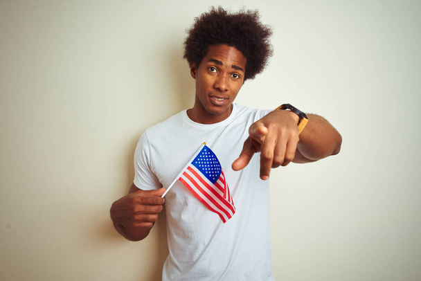 Afro man holding United Estates of America USA flag standing over isolated white background pointing with finger to the camera and to you, hand sign, positive and confident gesture from the front - Foto, Imagem