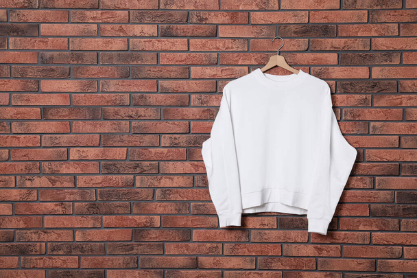 Hanger with new sweater on brick wall, mock up for design - Fotó, kép