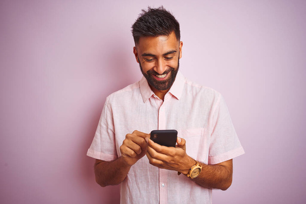 Young indian man using smartphone standing over isolated pink background with a happy face standing and smiling with a confident smile showing teeth - Foto, immagini