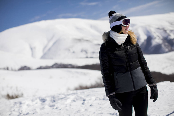 Jovem mulher fica em uma encosta de montanha nevada em seu terno de esqui no dia
 - Foto, Imagem
