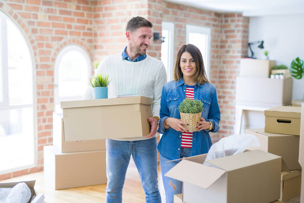 Young beautiful couple standing at new home around cardboard boxes  - Photo, Image