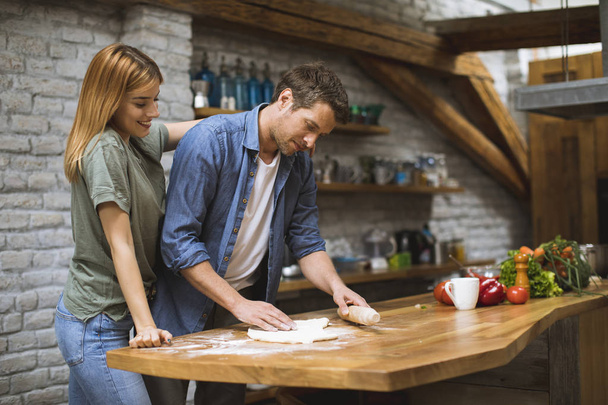 Jovem casal alegre fazendo pizza na cozinha rústica juntos
 - Foto, Imagem