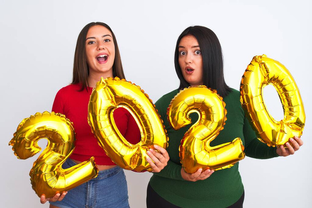 Giovani belle donne sorridenti felici e fiduciosi che celebrano il nuovo anno. In piedi con il sorriso sul viso tenendo palloncini fare il numero 2020
 - Foto, immagini