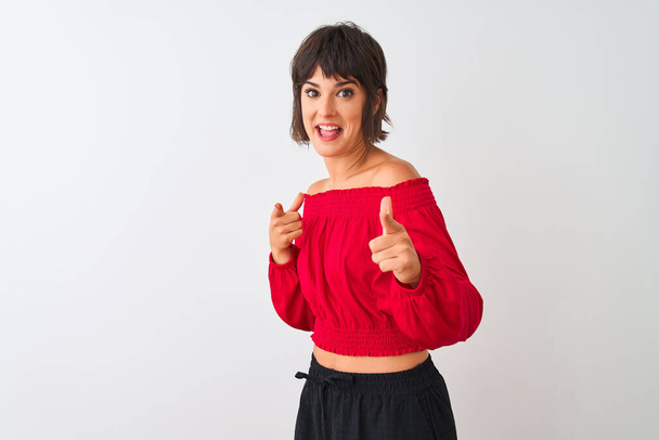 Jonge mooie vrouw draagt rode zomer t-shirt staan over geïsoleerde witte achtergrond wijzende vingers naar camera met gelukkig en grappig gezicht. Goede energie en vibraties. - Foto, afbeelding