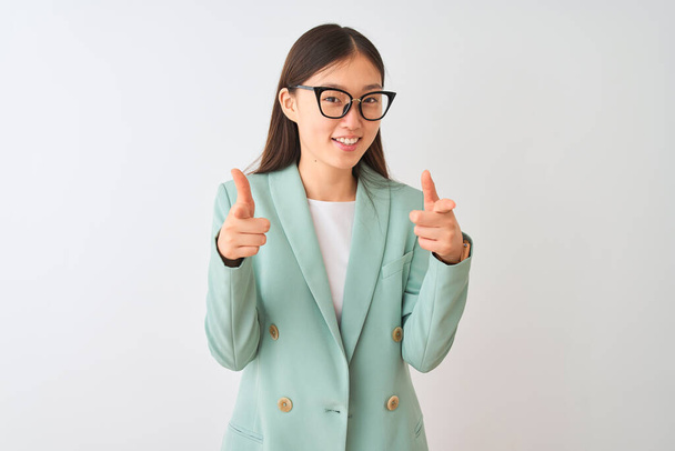 Empresária chinesa vestindo jaqueta elegante e óculos sobre fundo branco isolado apontando dedos para a câmera com rosto feliz e engraçado. Boa energia e vibrações
. - Foto, Imagem