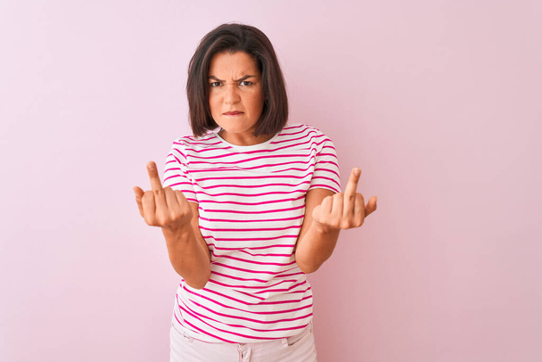 junge schöne Frau in gestreiftem T-Shirt, das über isoliertem rosa Hintergrund steht und den Mittelfinger zeigt, wie sie dich fickt, schlechte Miene, Provokation und unhöfliche Haltung zeigt. Kreischen erregt - Foto, Bild