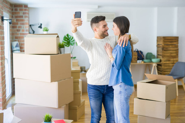 Όμορφο ζευγάρι παίρνοντας μια φωτογραφία selfie χρησιμοποιώντας smartphone σε νέο διαμέρισμα, χαμογελαστή χαρούμενη για το νέο σπίτι - Φωτογραφία, εικόνα