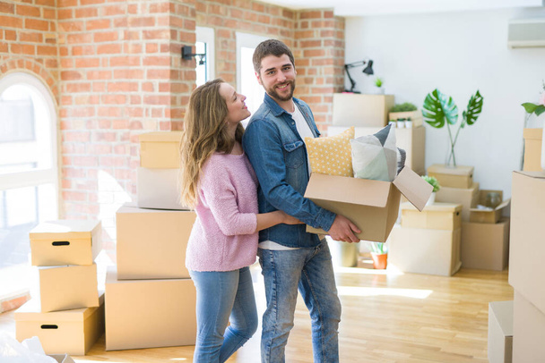 Young beautiful couple very happy together holding cardboard boxes moving to a new home - Photo, Image