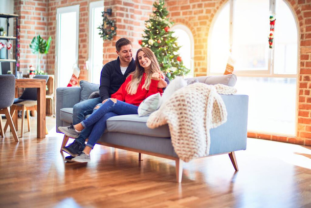 Young beautiful couple smiling happy and confident. Sitting on the sofa hugging around christmas tree at home - Foto, Imagen
