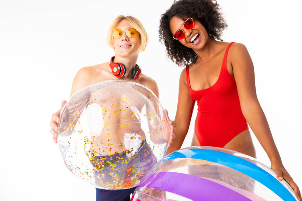 African woman and Caucasian blonde man in swimwear posing with rubber balls against white background  - Photo, Image