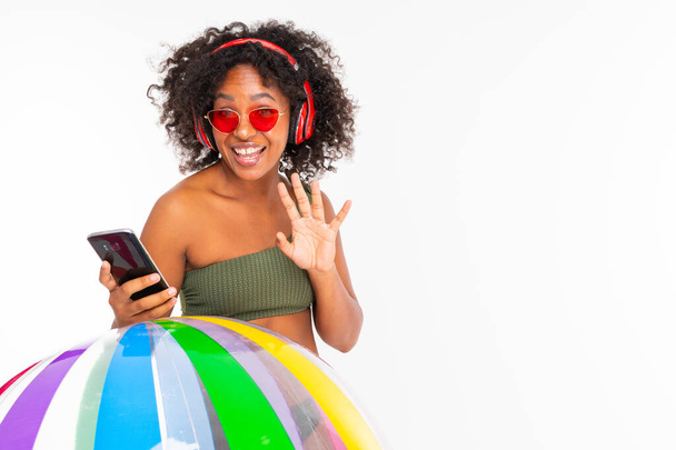 African woman in swimwear posing with inflatable ball and mobile phone against white background  - Fotó, kép