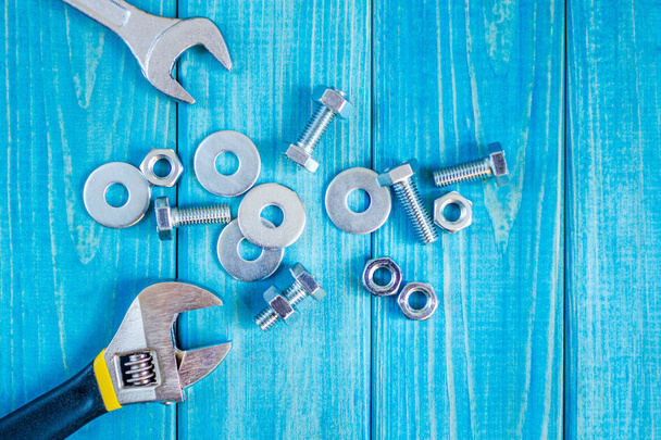 Metallschrauben und Muttern auf blauem Holzhintergrund mit verstellbarem Schraubenschlüssel - Foto, Bild