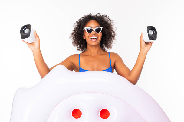 Afrikanerin in Badebekleidung posiert mit Luftmatratze und Lautsprechern vor weißem Hintergrund  - Foto, Bild