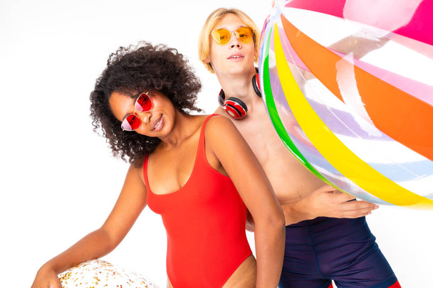African woman and Caucasian blonde man in swimwear posing with rubber balls against white background  - Photo, Image