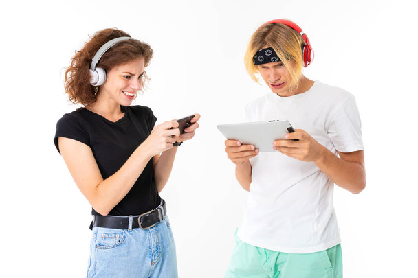 Woman with mobile phone and man with digital tablet posing in headphones against white background   - Photo, Image