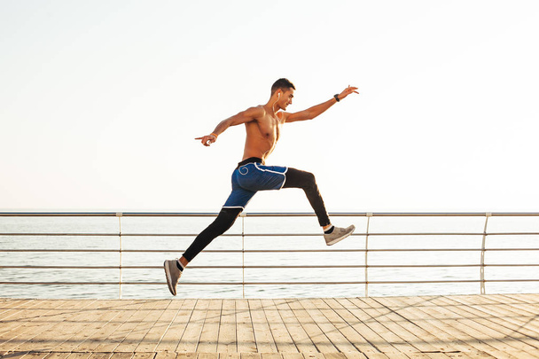 Sportlicher Kerl macht einen Sprung in die Luft vor dem Hintergrund des Meeres - Foto, Bild