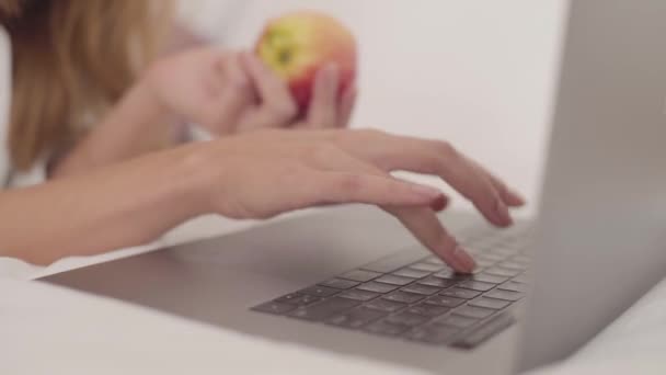 Close-up of a young Caucasian female hand typing on laptop. Woman holding the red apple in the other hand at the background. - Imágenes, Vídeo