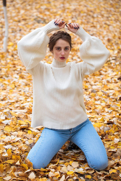Young beautiful girl in blue jeans and gwhite sweater  - Фото, изображение