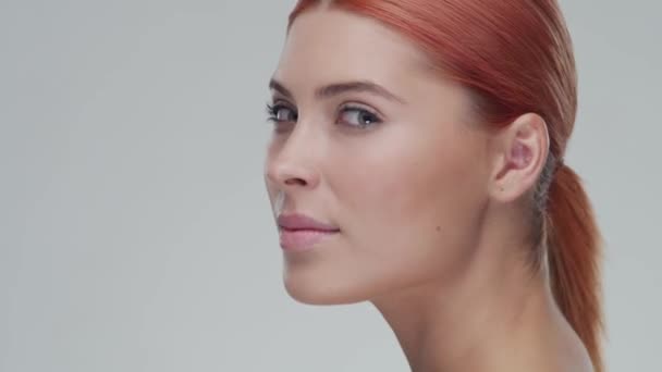 Studio portrait of young, beautiful and natural redhead woman applying skin care cream. Face lifting, cosmetics and make-up. - Кадры, видео