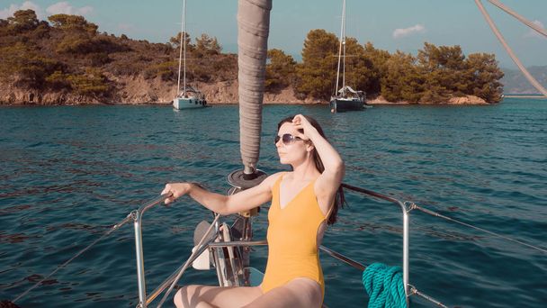 Brunette girl in one piece swimsuit posing on the bow of a sailing yacht, - Φωτογραφία, εικόνα