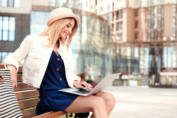 Beautiful woman using laptop on bench in city - Фото, изображение