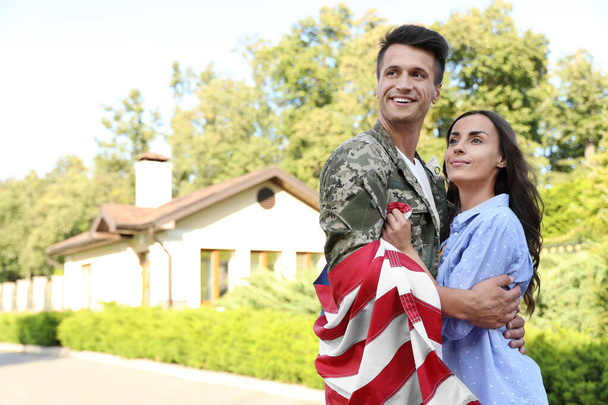 Mies armeijan univormussa, jonka lippu halaa hänen vaimoaan ulkona.
 - Valokuva, kuva
