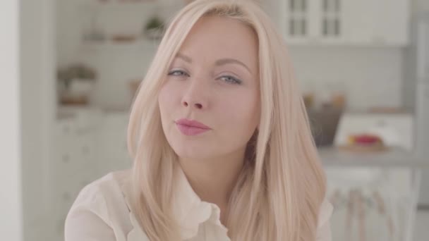 Close-up face of a Caucasian blond woman with grey eyes looking at the camera and smiling. Happy lady posing on weekends at home. - Materiał filmowy, wideo