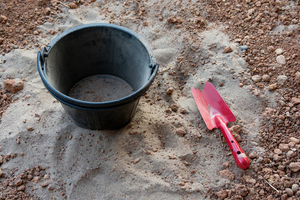 Κόκκινο φτυάρι και μαύρο πλαστικό κουβά στην άμμο - Φωτογραφία, εικόνα