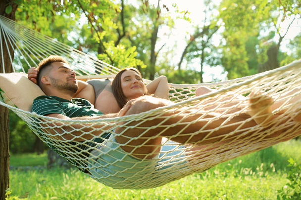 Young couple resting in comfortable hammock at green garden - Fotó, kép
