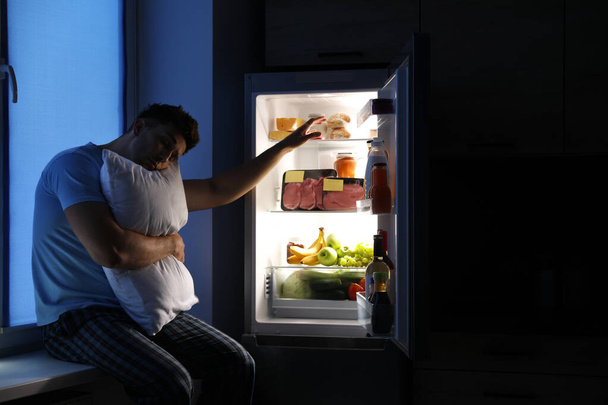 Uomo assonnato con cuscino vicino al frigorifero in cucina di notte
 - Foto, immagini