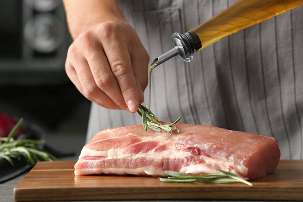 Man cooking fresh raw meat with oil and rosemary on wooden board, closeup - Фото, изображение