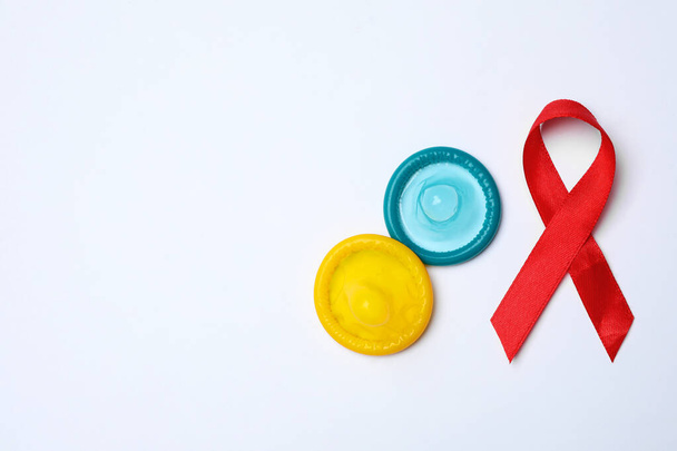 Colorful condoms and red ribbon on white background, top view. LGBT concept - Фото, изображение