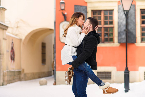Young healthy man holds his pretty girlfriend on the hands on background of winter snowy street. New Year and Christmas concept. - Fotografie, Obrázek