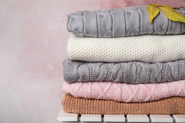 Stack of warm knitted clothes and autumn leaves on white wooden table against pink background - Fotoğraf, Görsel