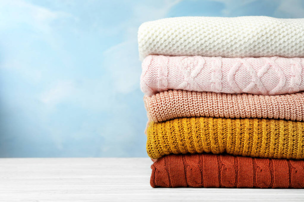 Stack of warm clothes on white wooden table against light blue background, space for text. Autumn season - Photo, Image