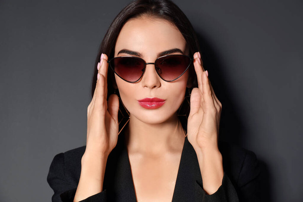 Beautiful woman wearing jacket and sunglasses on black background - Photo, image