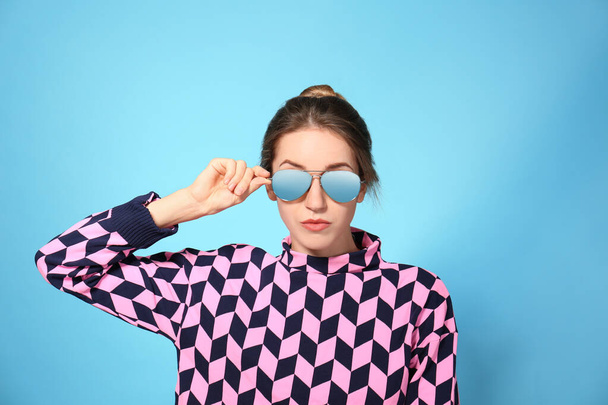 Young woman wearing stylish sunglasses on blue background - 写真・画像