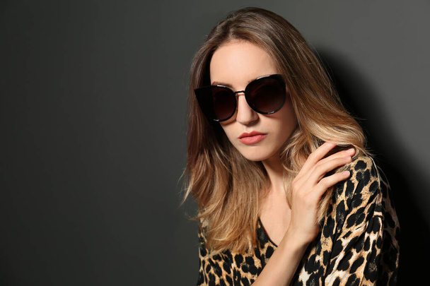 Young woman wearing stylish sunglasses on dark grey background. Space for text - Foto, afbeelding