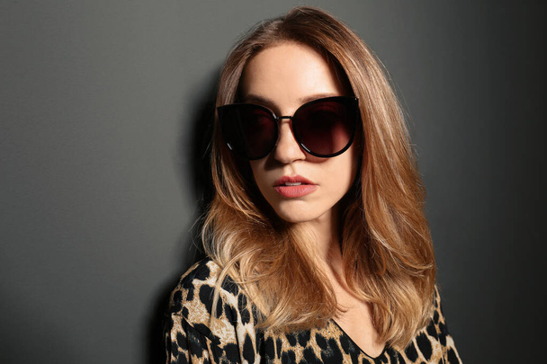 Young woman wearing stylish sunglasses on dark grey background - Foto, Bild